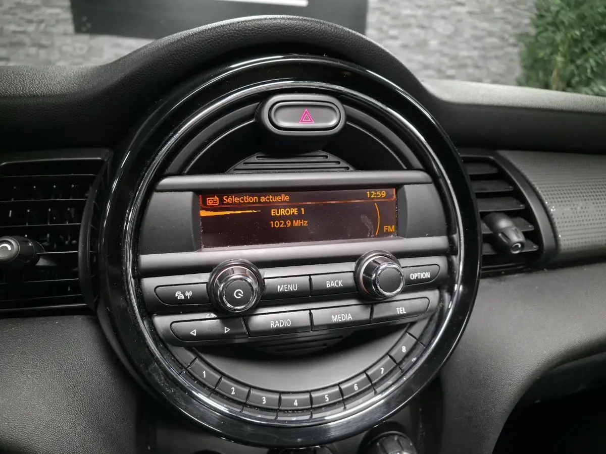 Gros plan sur la console centrale noire du MINI Cabriolet bleu, affichant l'autoradio réglé sur Europe 1 à 102.9 MHz.