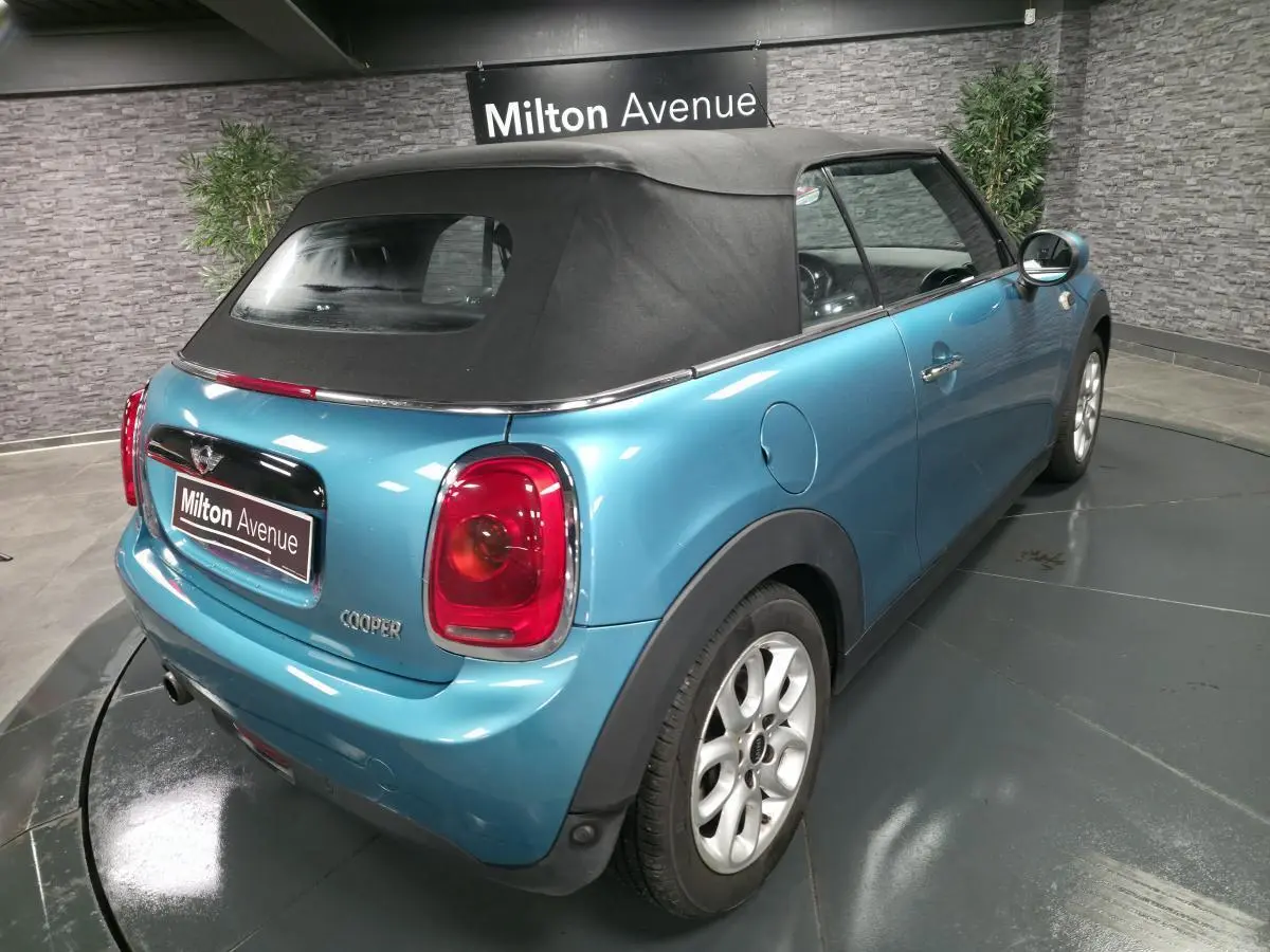 Vue 3/4 arrière droite d'une MINI Cabriolet bleu avec capote noire et feux arrière rouges, stationnée en intérieur.