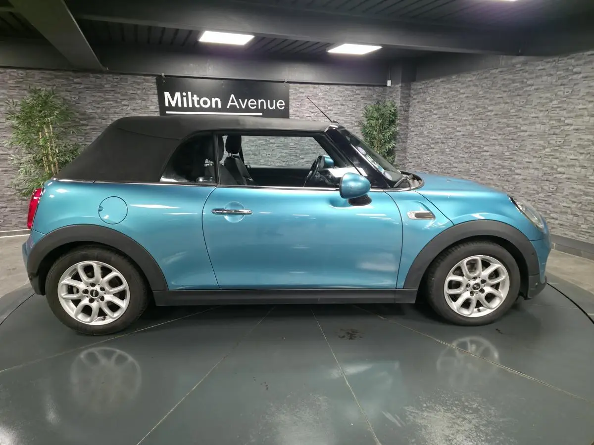 Vue de profil côté gauche d'une MINI Cabriolet bleu avec capote noire et jantes argentées en intérieur showroom.