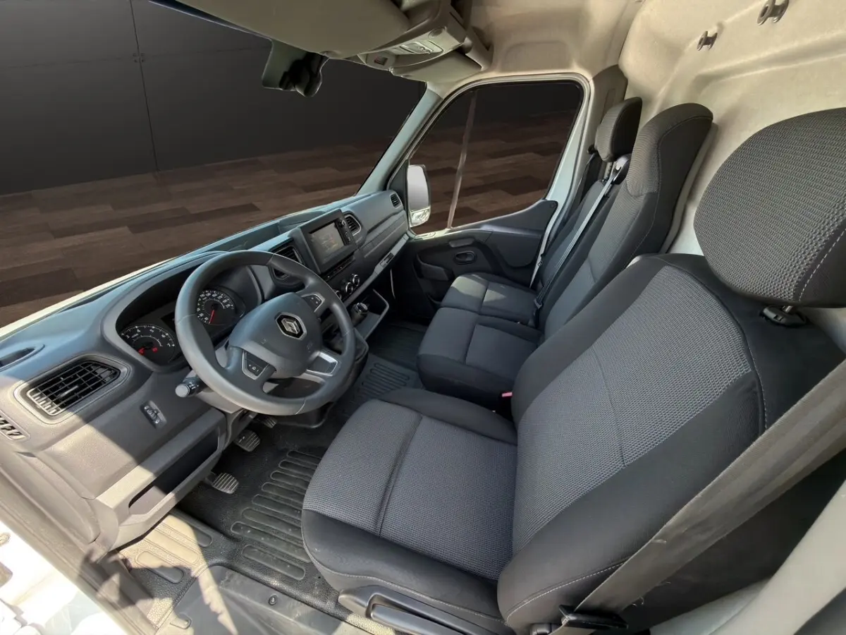 Vue intérieure côté conducteur du Renault Master blanc 2023, montrant le tableau de bord et les sièges noirs.
