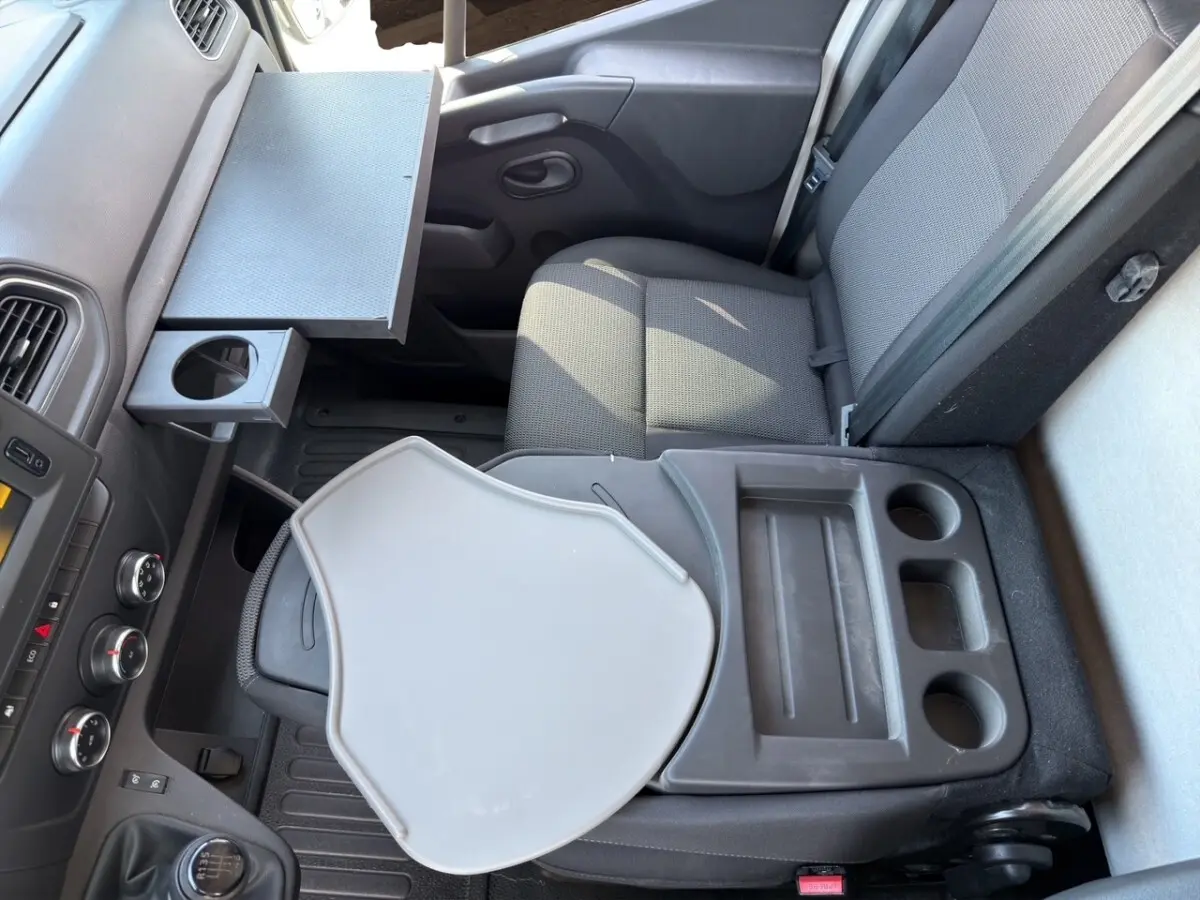 Vue intérieure côté passager du Renault Master 2023, montrant siège gris avec tablette rabattable et rangements intégrés.