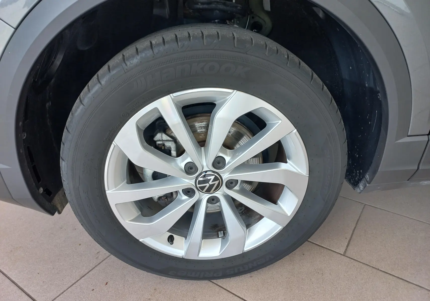 Gros plan sur la roue avant gauche du Volkswagen T-Roc 2025 gris Indium, mettant en valeur la jante alliage et le pneu Hankook.