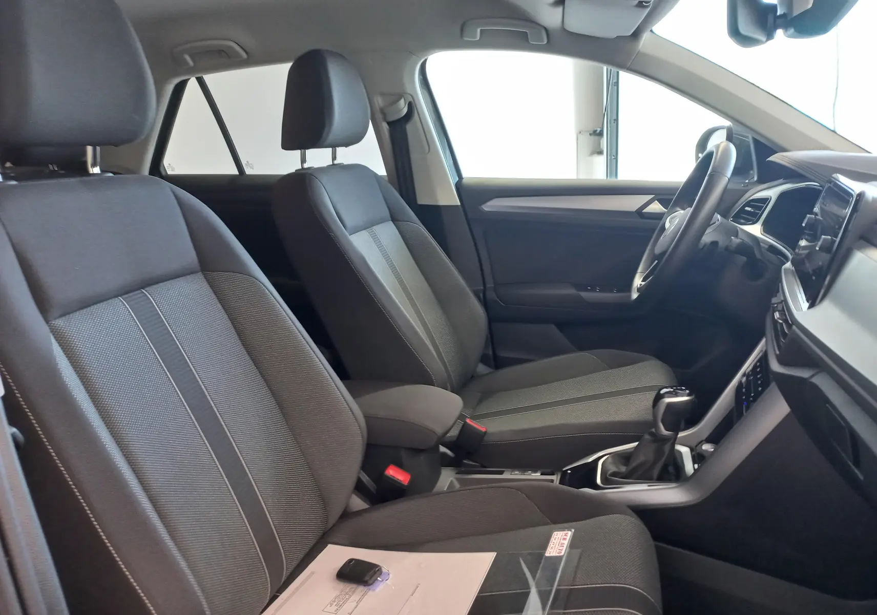 Vue intérieure côté gauche du Volkswagen T-Roc 2025, sièges tissu gris avec console centrale et volant visibles.
