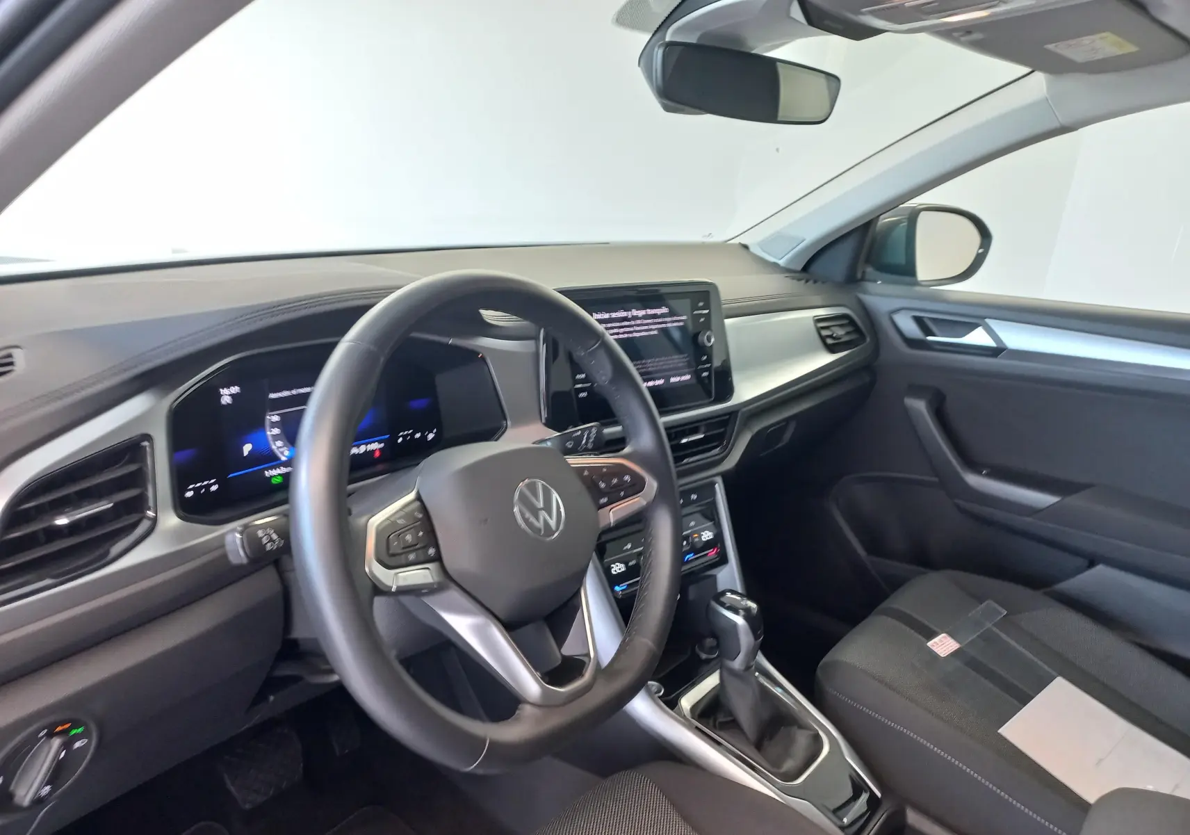 Vue intérieure côté conducteur du Volkswagen T-Roc 2025 gris Indium, avec tableau de bord digital et volant multifonction.