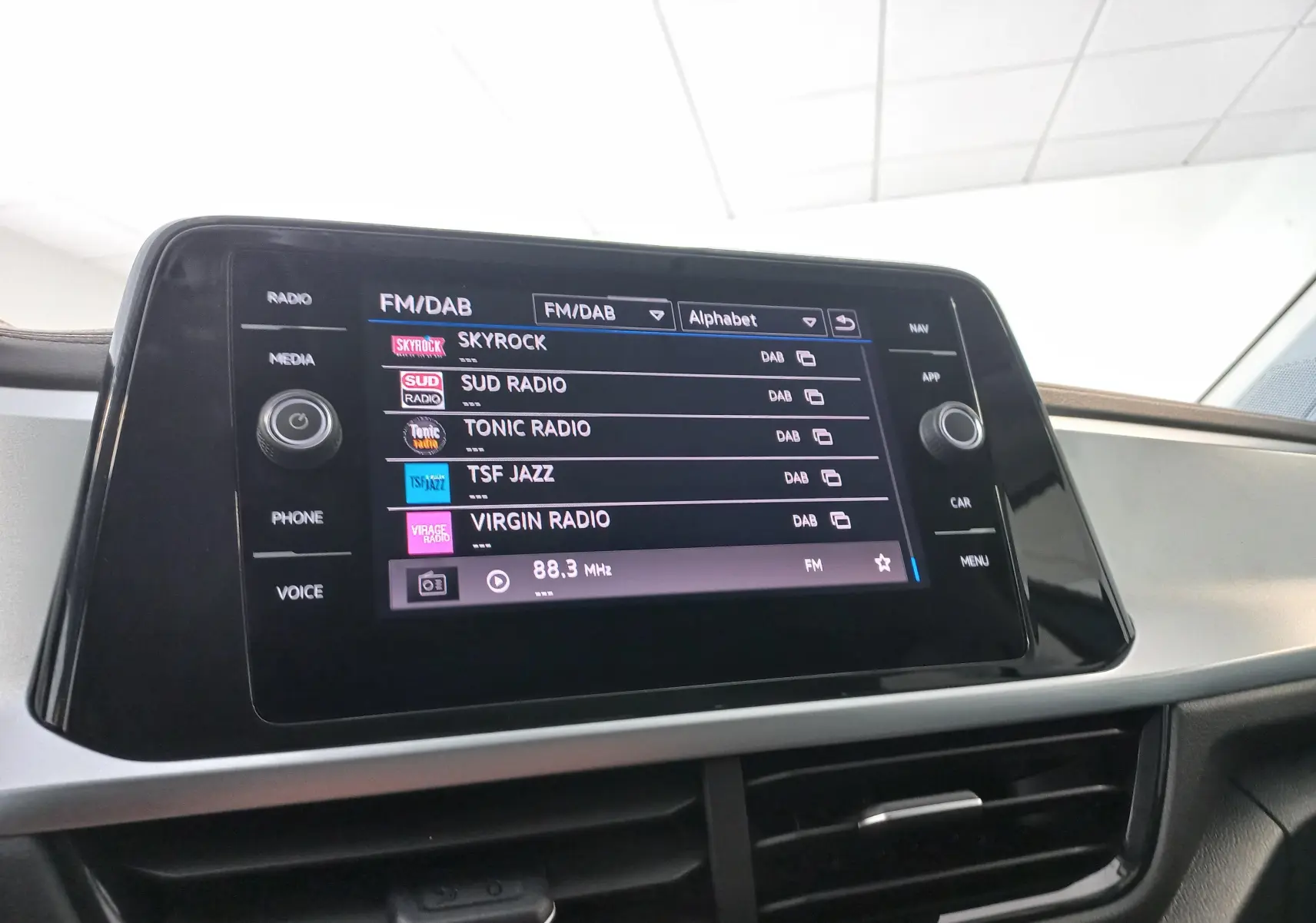 Écran tactile central du Volkswagen T-Roc 2025 gris Indium, affichant les stations radio FM/DAB en intérieur.