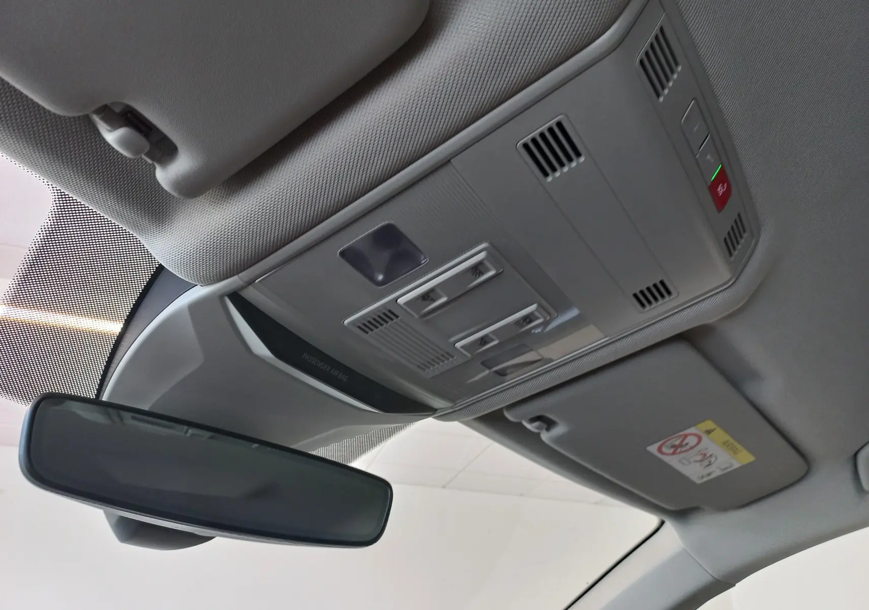 Vue intérieure du plafond avant du Volkswagen T-Roc 2025 gris Indium, montrant le miroir de courtoisie et les commandes d'éclairage.