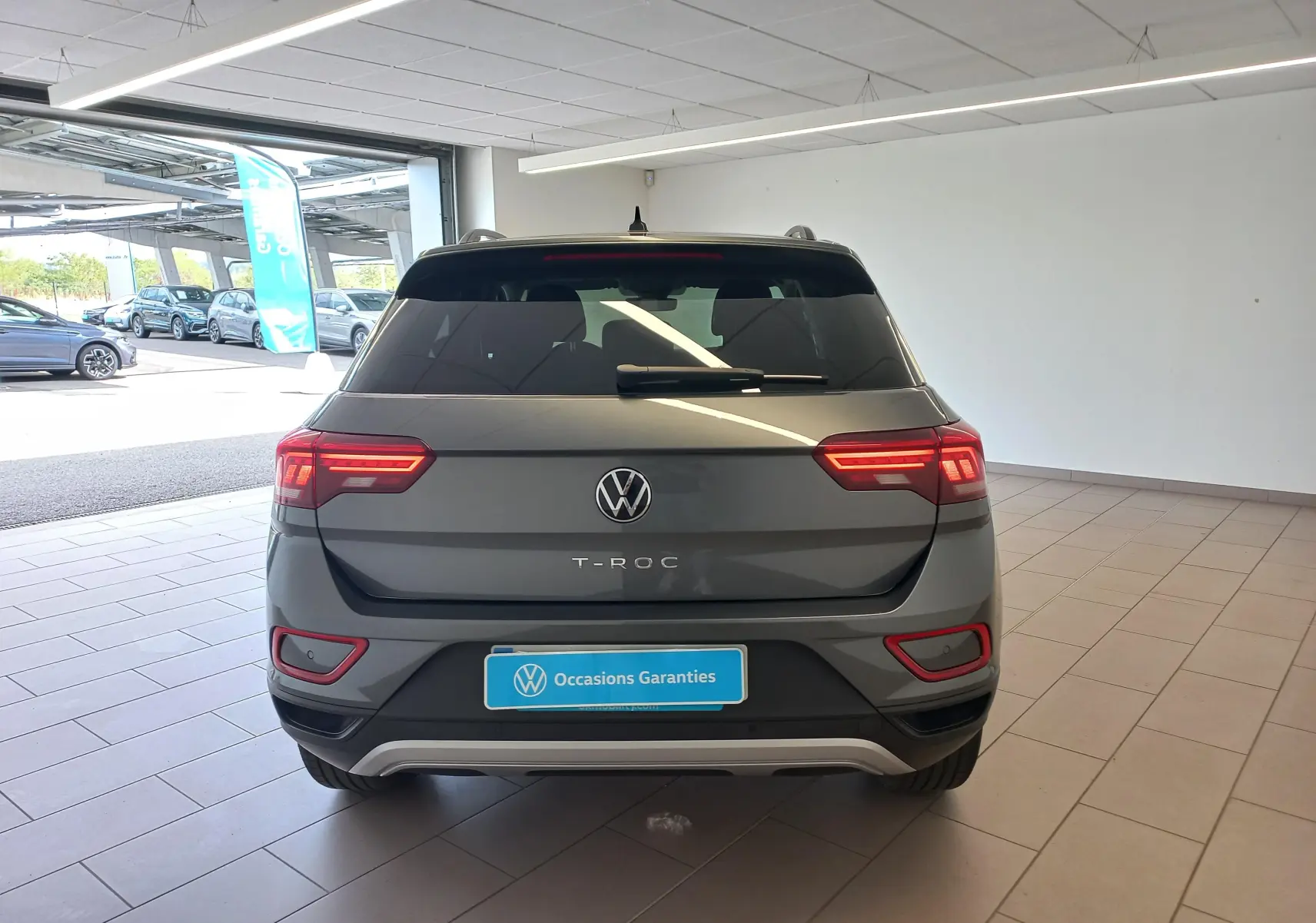 Vue arrière d'un Volkswagen T-Roc gris Indium 2025, avec feux LED allumés et badge T-ROC visible au centre.