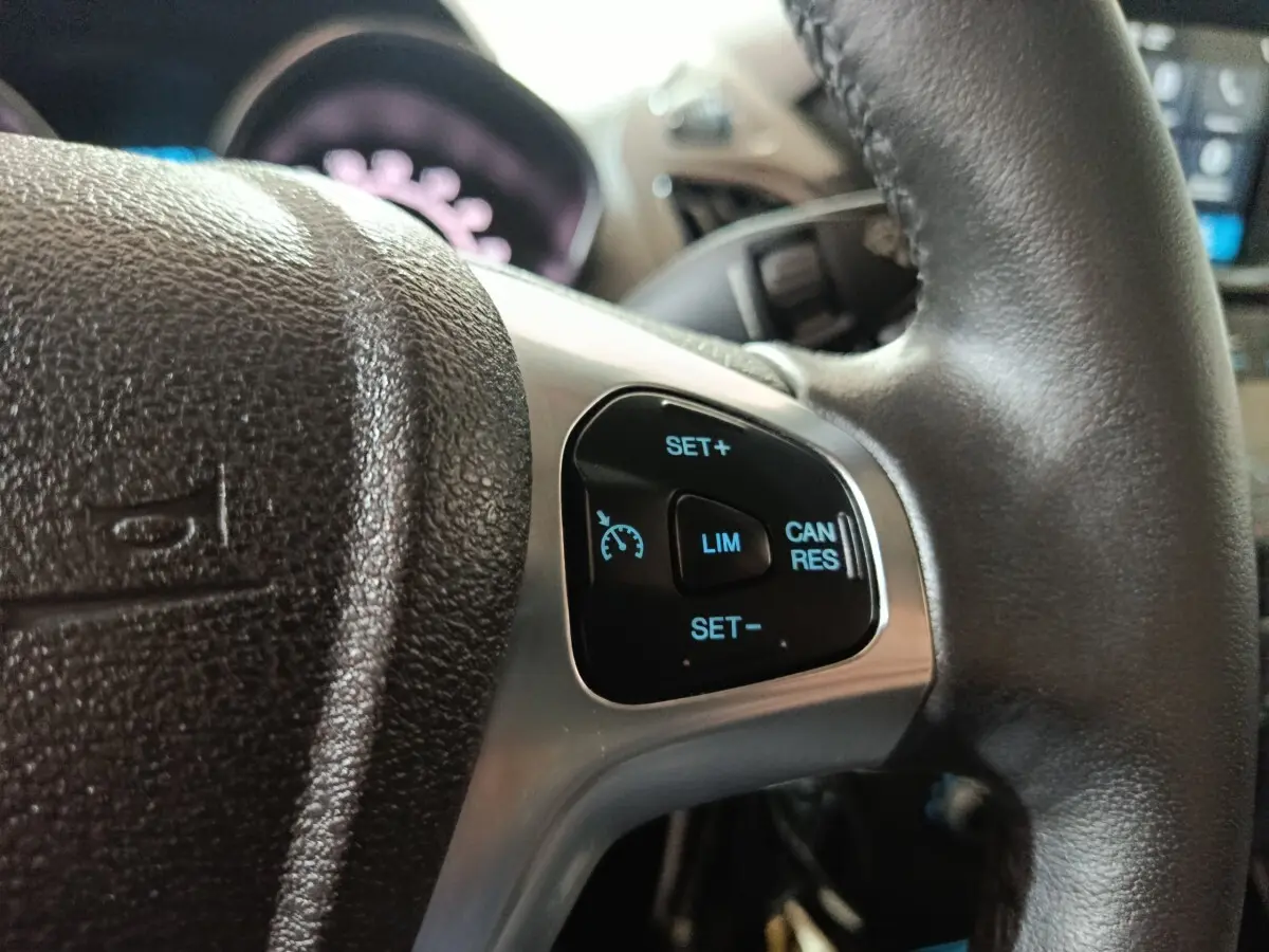 Gros plan sur les commandes du régulateur de vitesse au volant cuir noir du Ford Grand Tourneo Connect blanc.