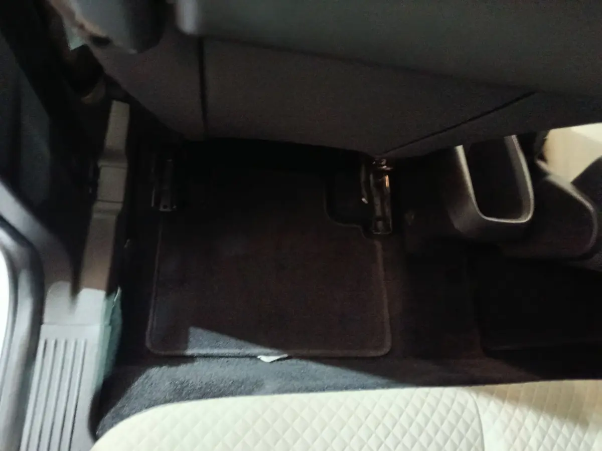 Vue rapprochée du plancher côté passager avant avec tapis noir et siège en tissu clair à motifs losanges.