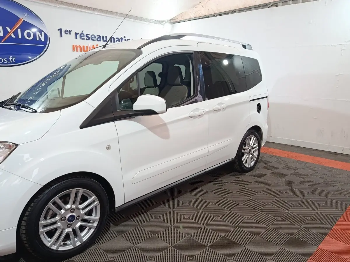 Vue côté gauche en 3/4 arrière d’un Ford Grand Tourneo Connect blanc, avec jantes alliage et vitres teintées.