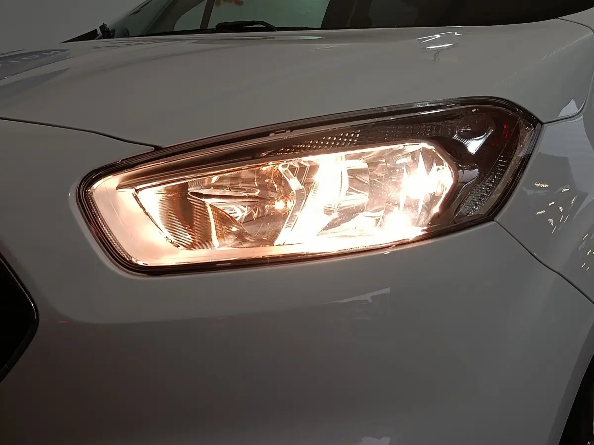 Gros plan sur le phare avant droit allumé d’un Ford Grand Tourneo Connect blanc, vue de face légèrement décalée.