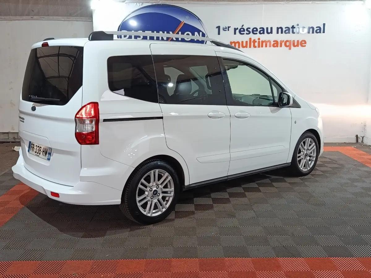 Ford Grand Tourneo Connect blanc vu en 3/4 arrière droit dans un showroom avec jantes alliage et vitres teintées.