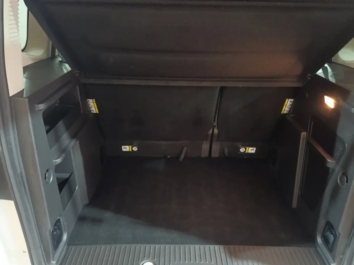 Coffre ouvert du Ford Grand Tourneo Connect blanc, vue intérieure arrière montrant l'espace de chargement noir.