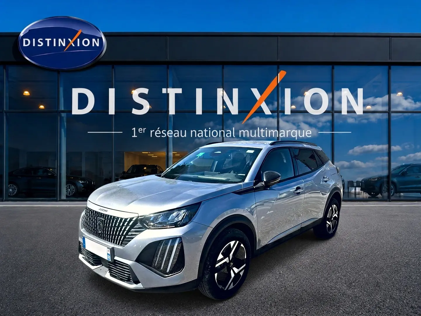Peugeot 2008 gris artense vue 3/4 avant droit, avec jantes alu et calandre distinctive devant un showroom Distinxion.