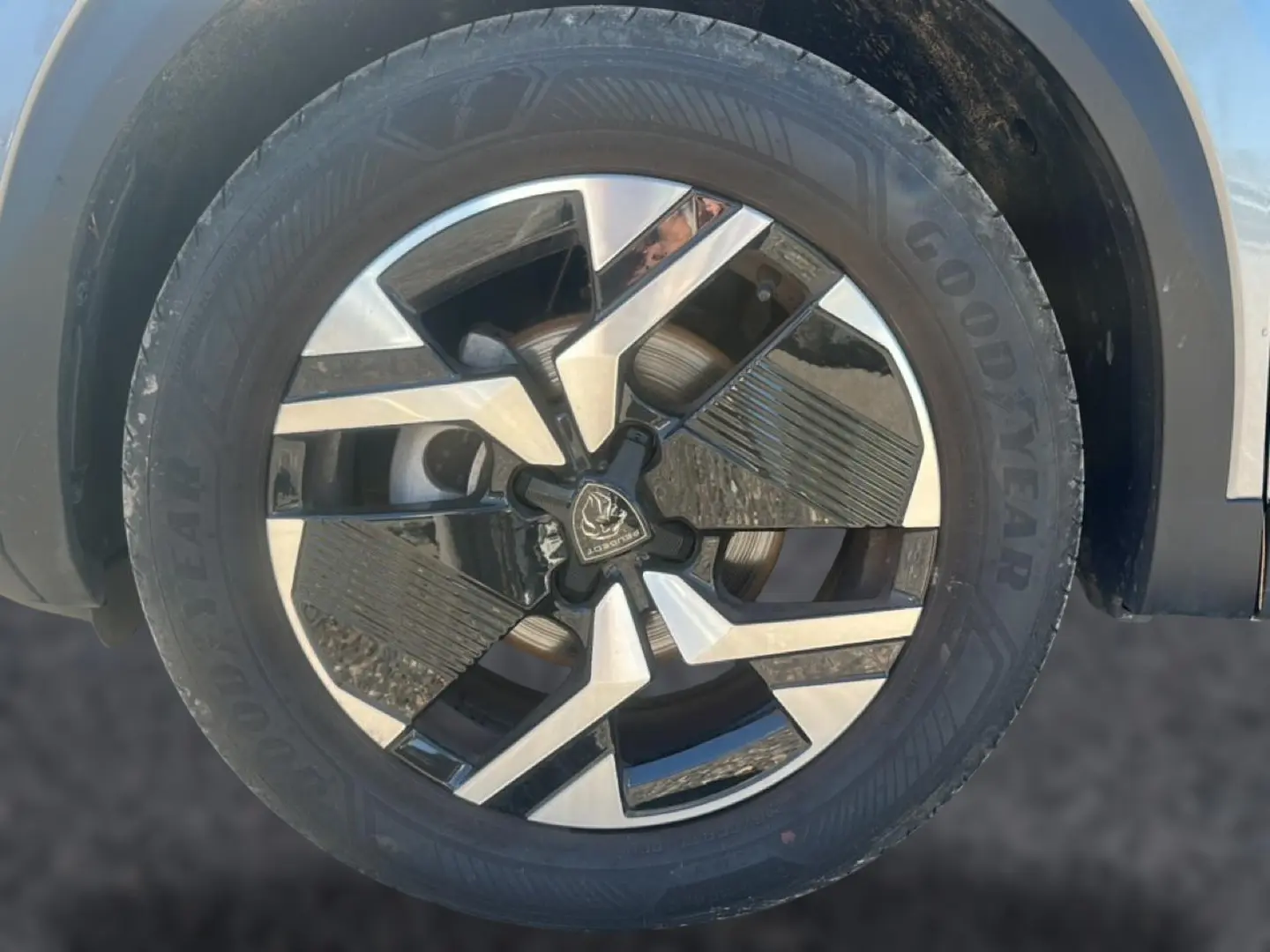 Gros plan sur la jante alu bicolore du côté avant droit d’un Peugeot 2008 gris Artense, pneu Goodyear visible.