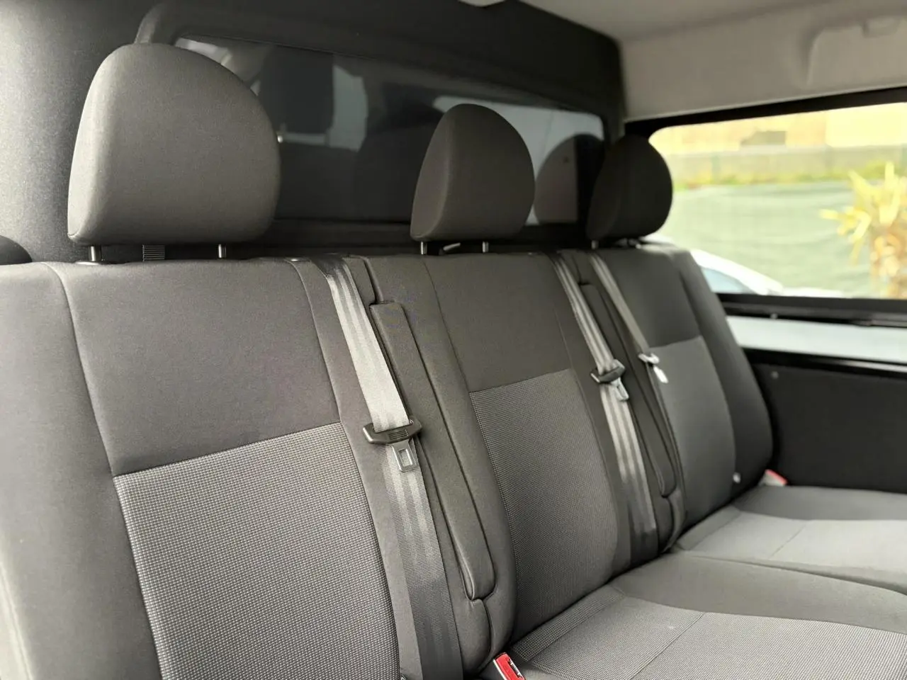 Vue intérieure du siège arrière trois places du Citroën Jumpy noir Perla avec appuie-têtes et ceintures visibles.