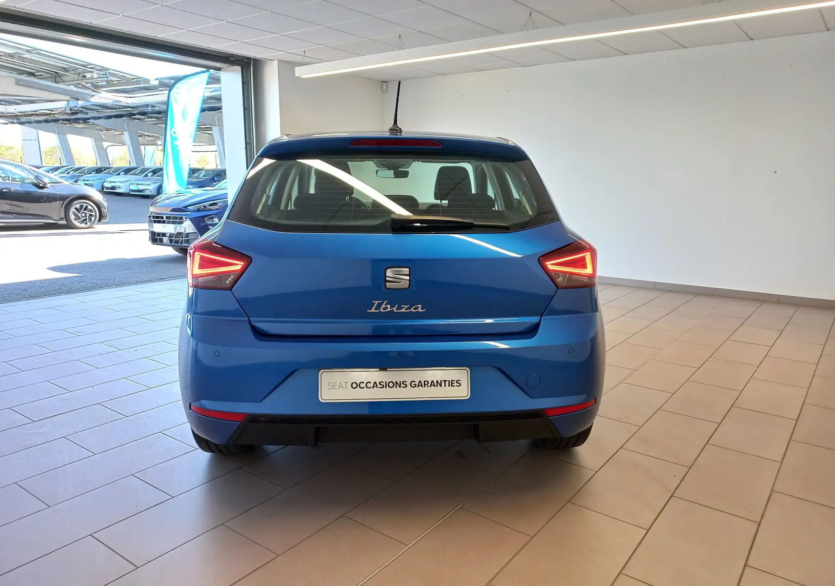 Vue arrière d'une SEAT Ibiza 2025 bleu saphir, avec feux arrière allumés, en showroom lumineux.