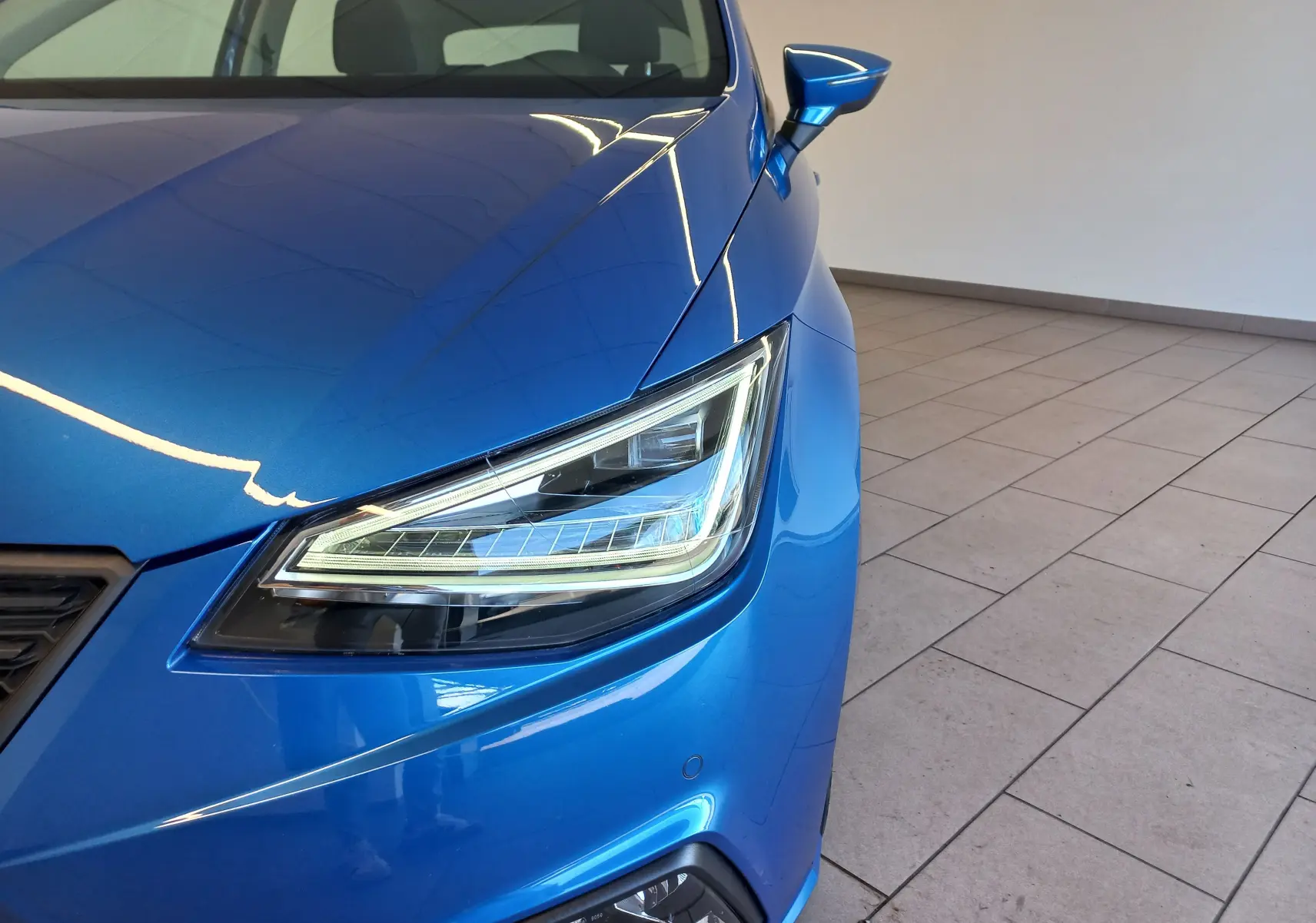 Gros plan sur l'avant droit bleu saphir du SEAT Ibiza 1.0 TSI 95 Copa 2025, mettant en valeur le phare LED et le rétroviseur.