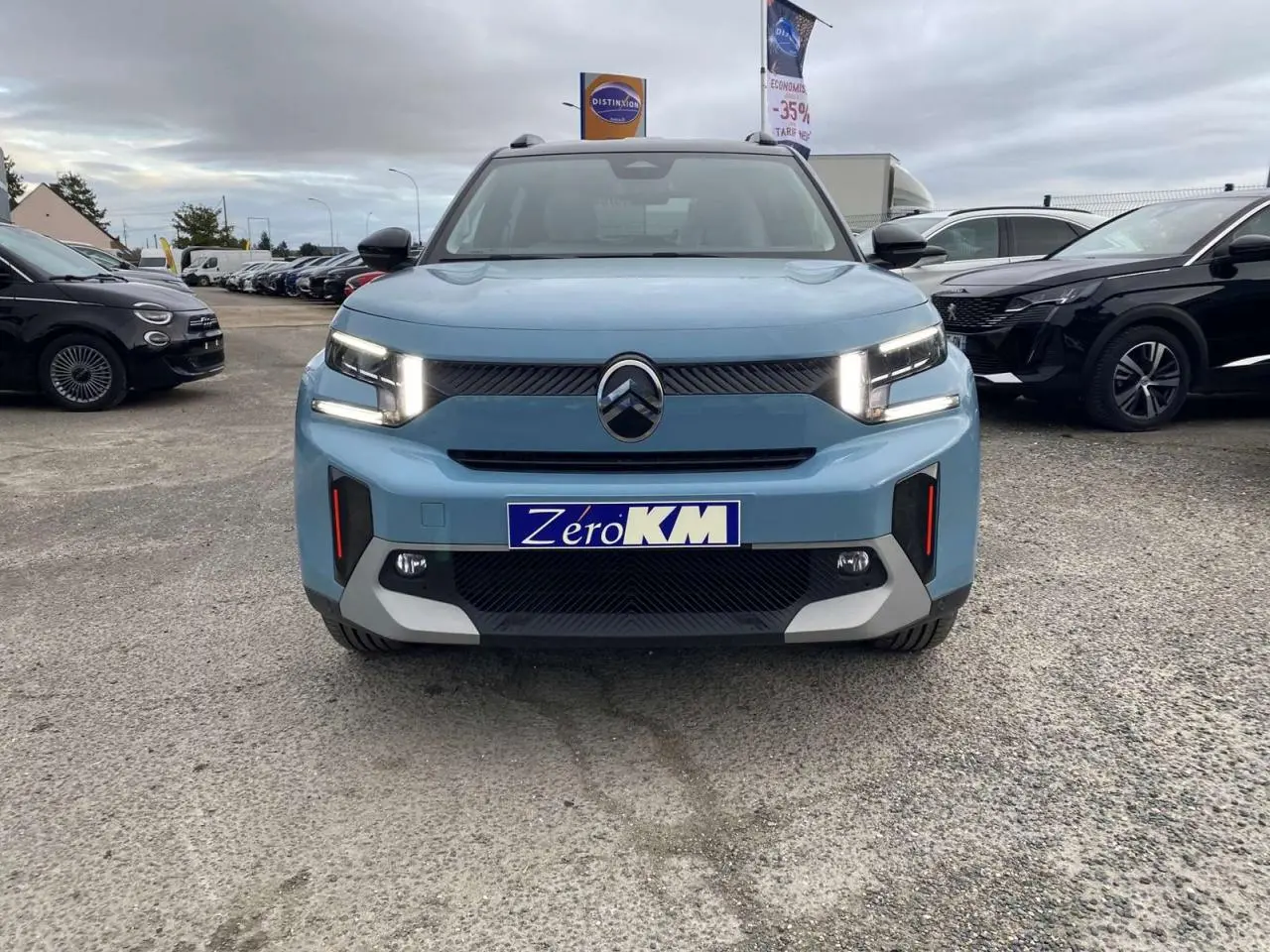 Vue avant d'une Citroën C3 Aircross hybride bleu Monte Carlo avec toit noir et feux LED allumés sur parking.