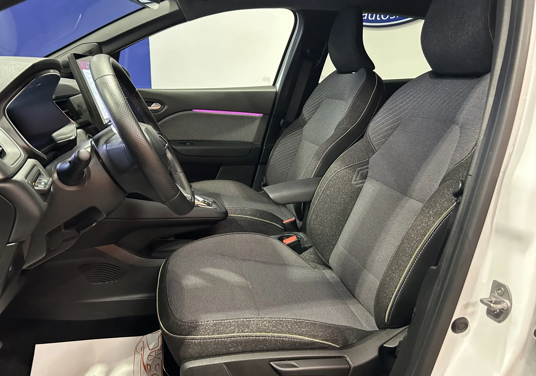 Vue intérieure côté conducteur de la Renault Symbioz E-Tech blanc nacré, sièges tissu gris et volant multifonction.