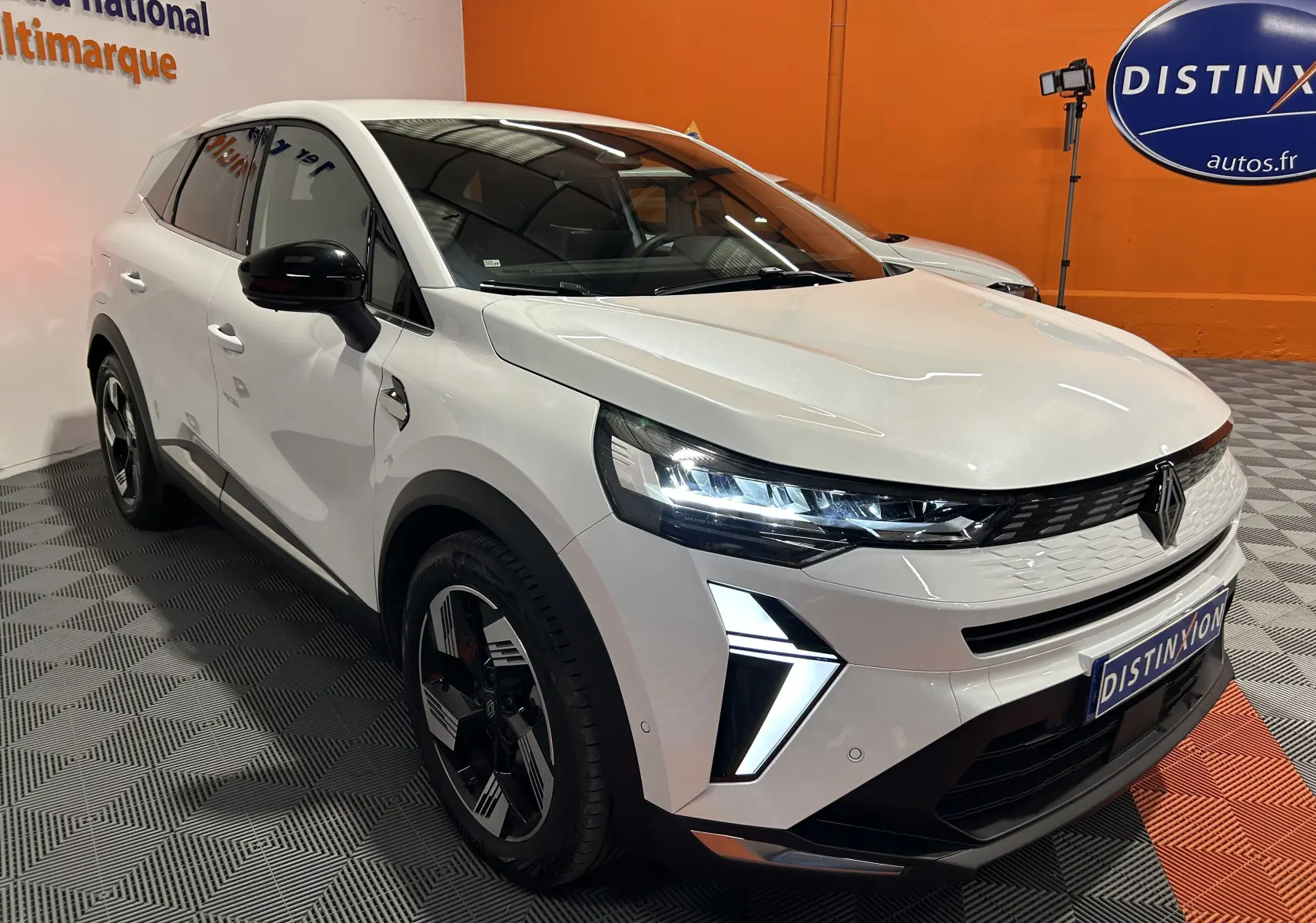 Vue 3/4 avant d'un Renault Symbioz blanc nacré avec feux LED allumés et jantes noires dans un showroom.