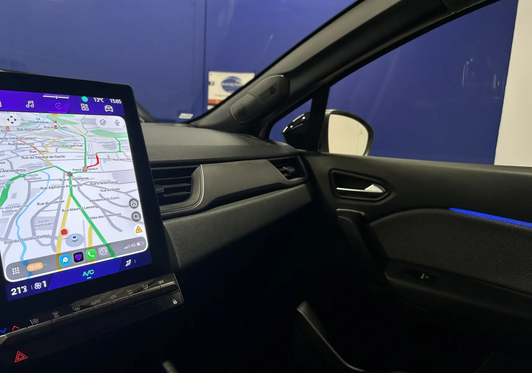 Vue intérieure côté passager du Renault Symbioz blanc nacré 2025, avec écran GPS tactile allumé et éclairage d'ambiance bleu.