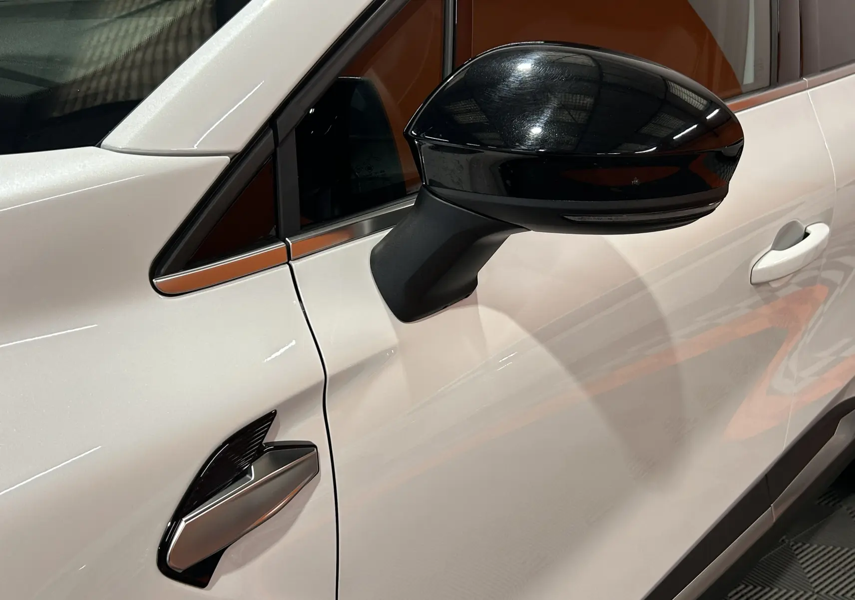 Gros plan sur la porte côté gauche d'une Renault Symbioz blanc nacré, avec rétroviseur noir brillant et poignée intégrée.