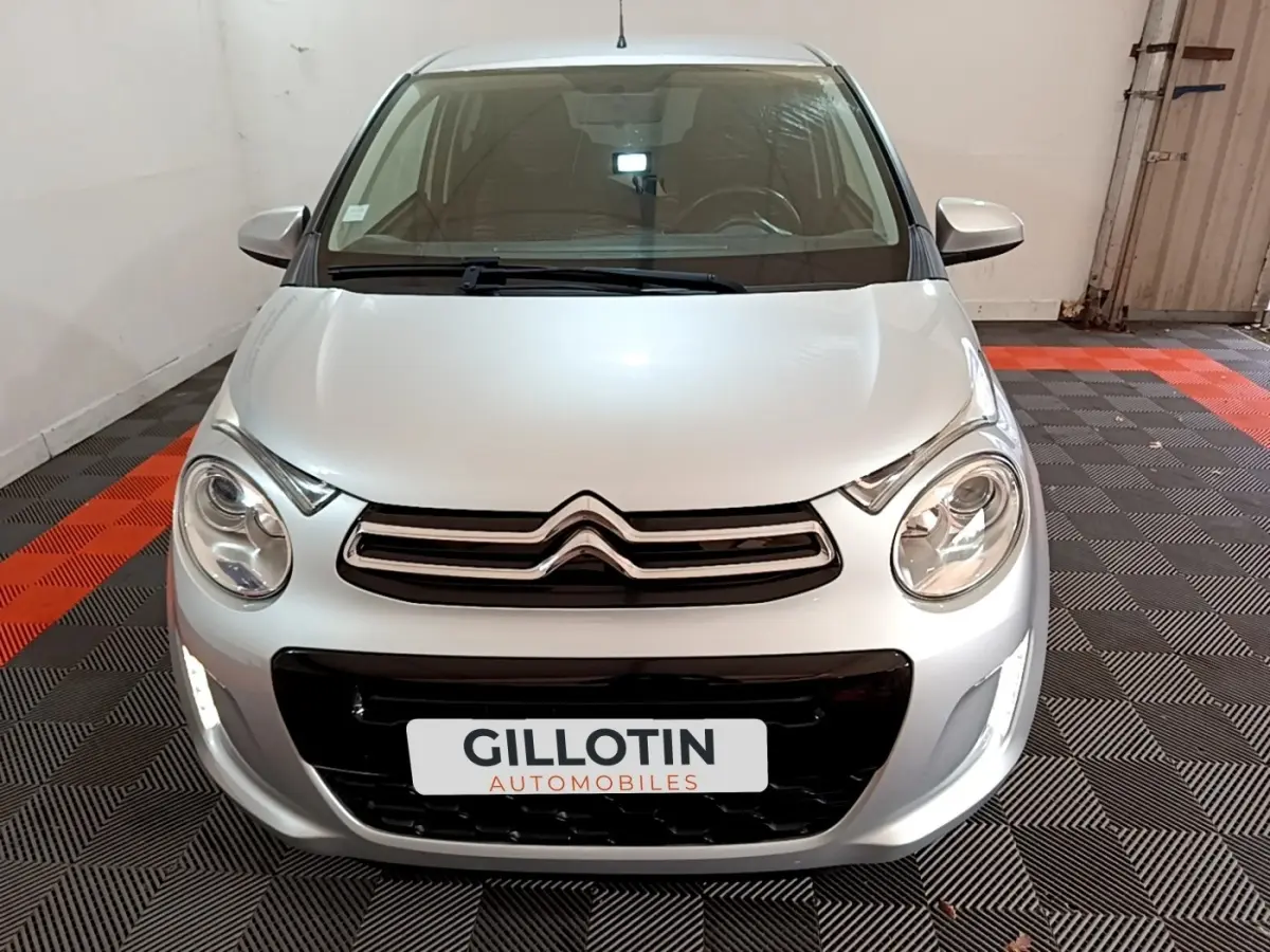 Vue avant d'une Citroën C1 gris clair 2019 avec phares ronds et calandre chromée dans un garage.
