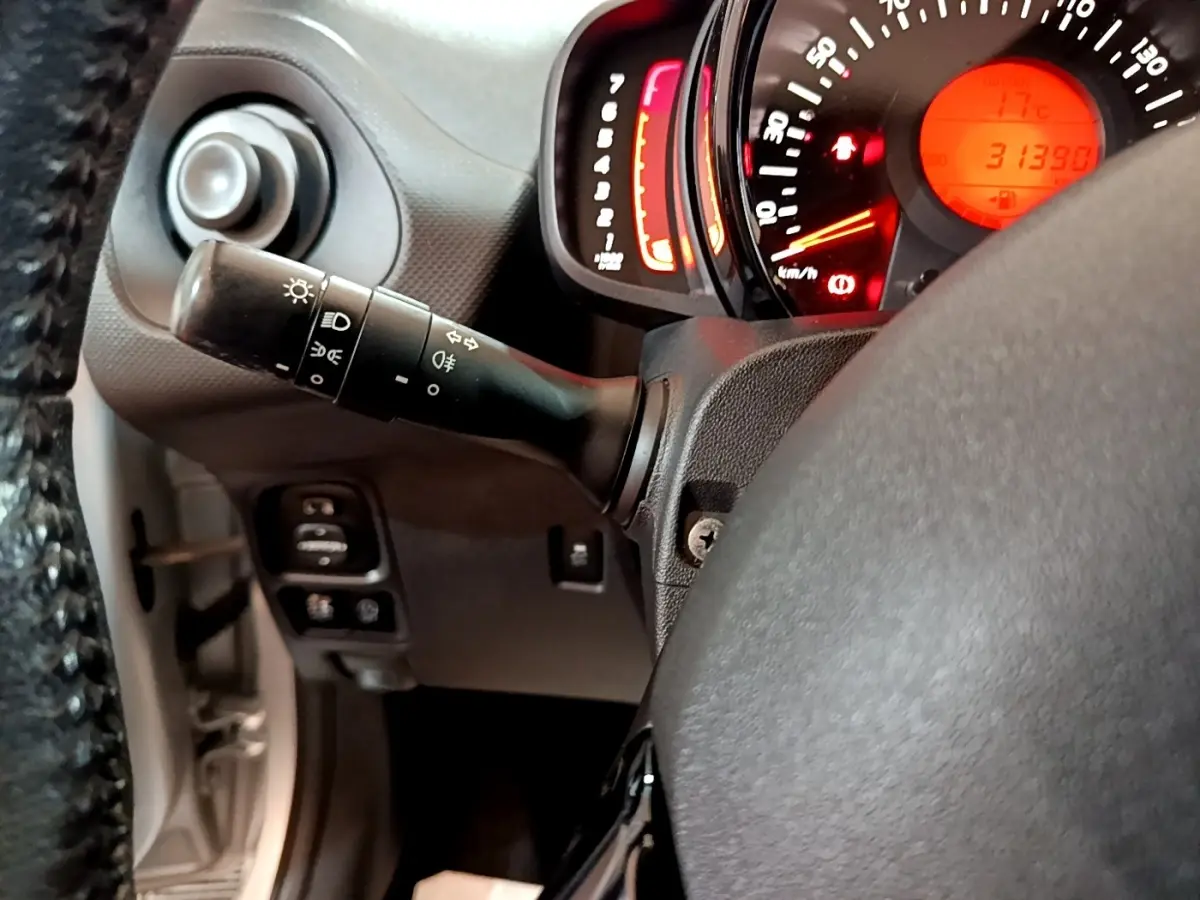 Vue rapprochée du commodo d’éclairage et du tableau de bord rougeoyant d’une Citroën C1 gris clair de 2019.