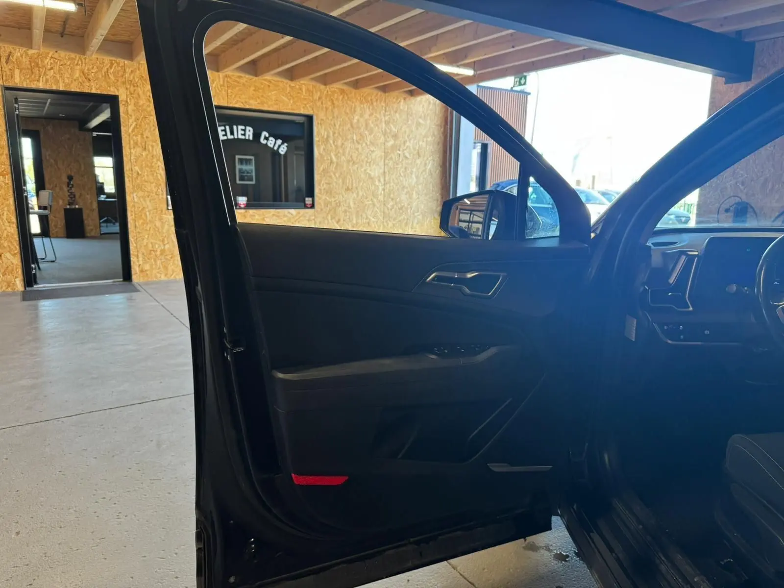 Vue intérieure côté gauche de la porte avant ouverte d’un KIA Sportage noir 2022, avec tableau de bord partiellement visible.