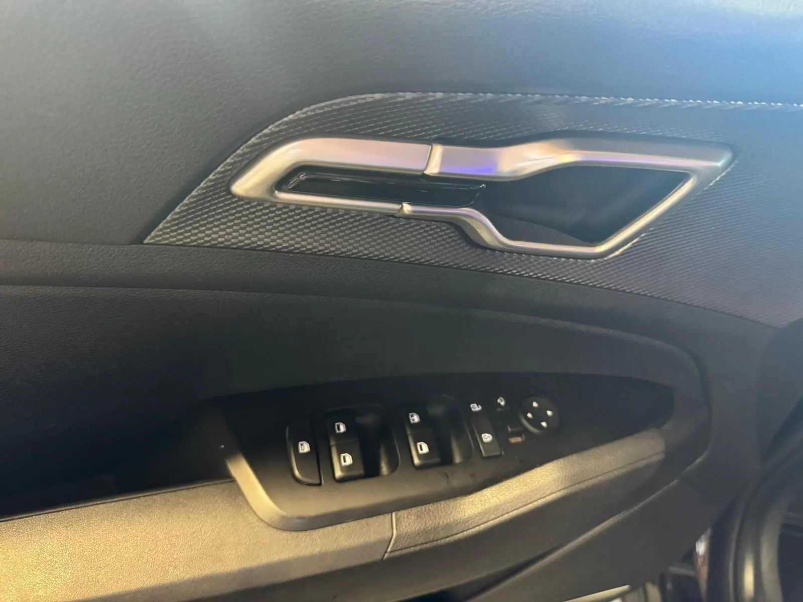 Gros plan sur la poignée intérieure et les commandes des vitres côté conducteur d’un KIA Sportage noir 2022.