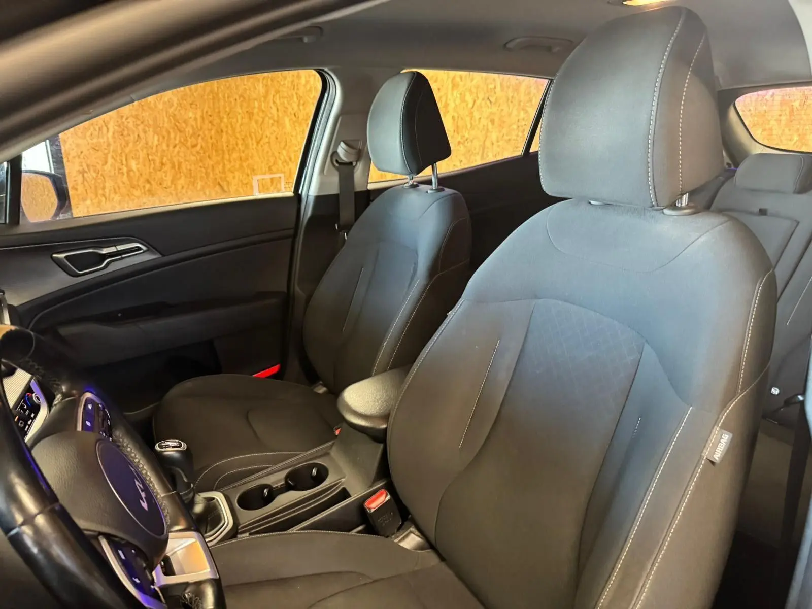 Vue intérieure côté conducteur du Kia Sportage 2022 noir, siège tissu noir avec coutures blanches et volant multifonction.