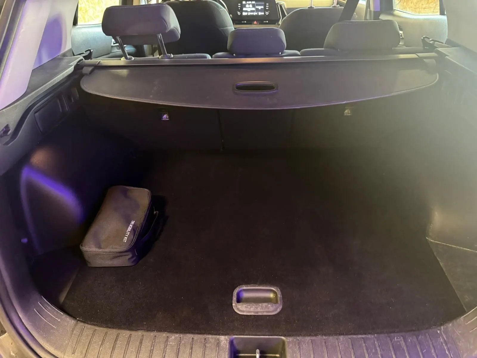 Vue intérieure du coffre noir du Kia Sportage 2022, avec cache-bagages et trousse de sécurité visible à gauche.