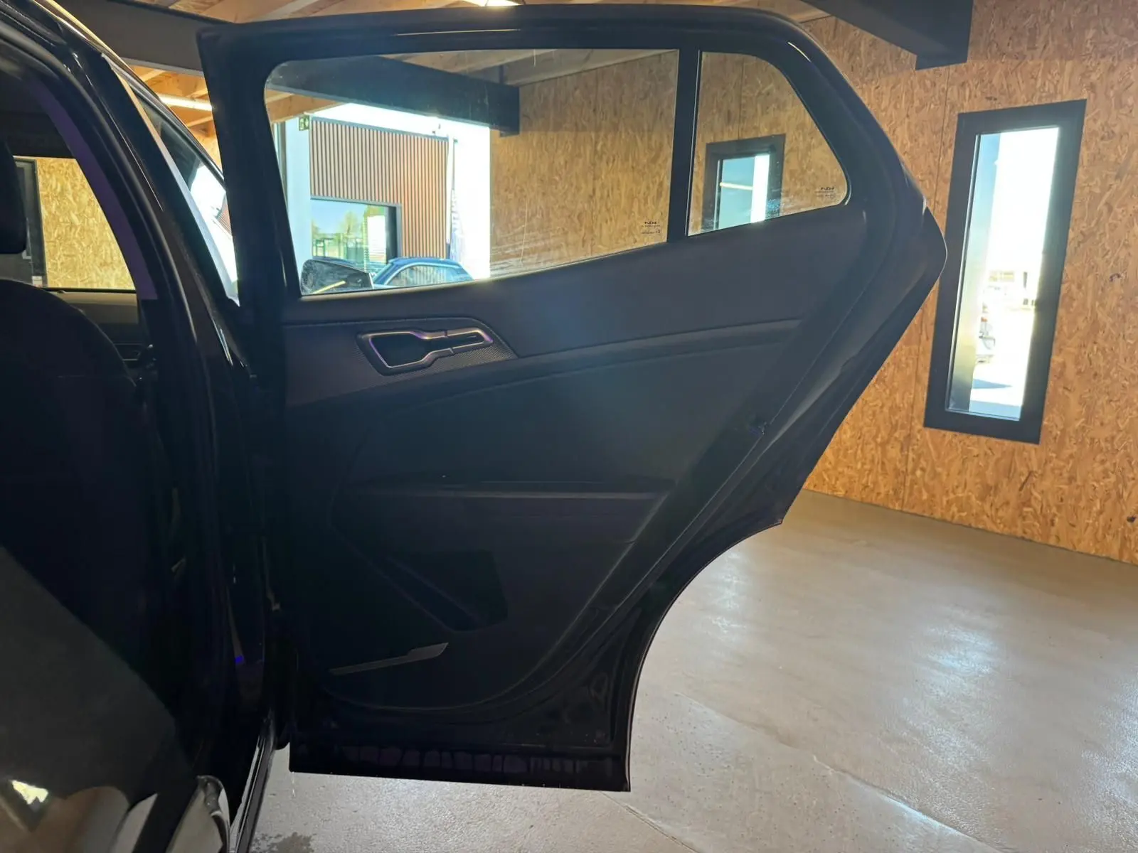 Vue intérieure sur la porte arrière gauche ouverte du Kia Sportage noir 2022, mettant en valeur les finitions intérieures sombres.
