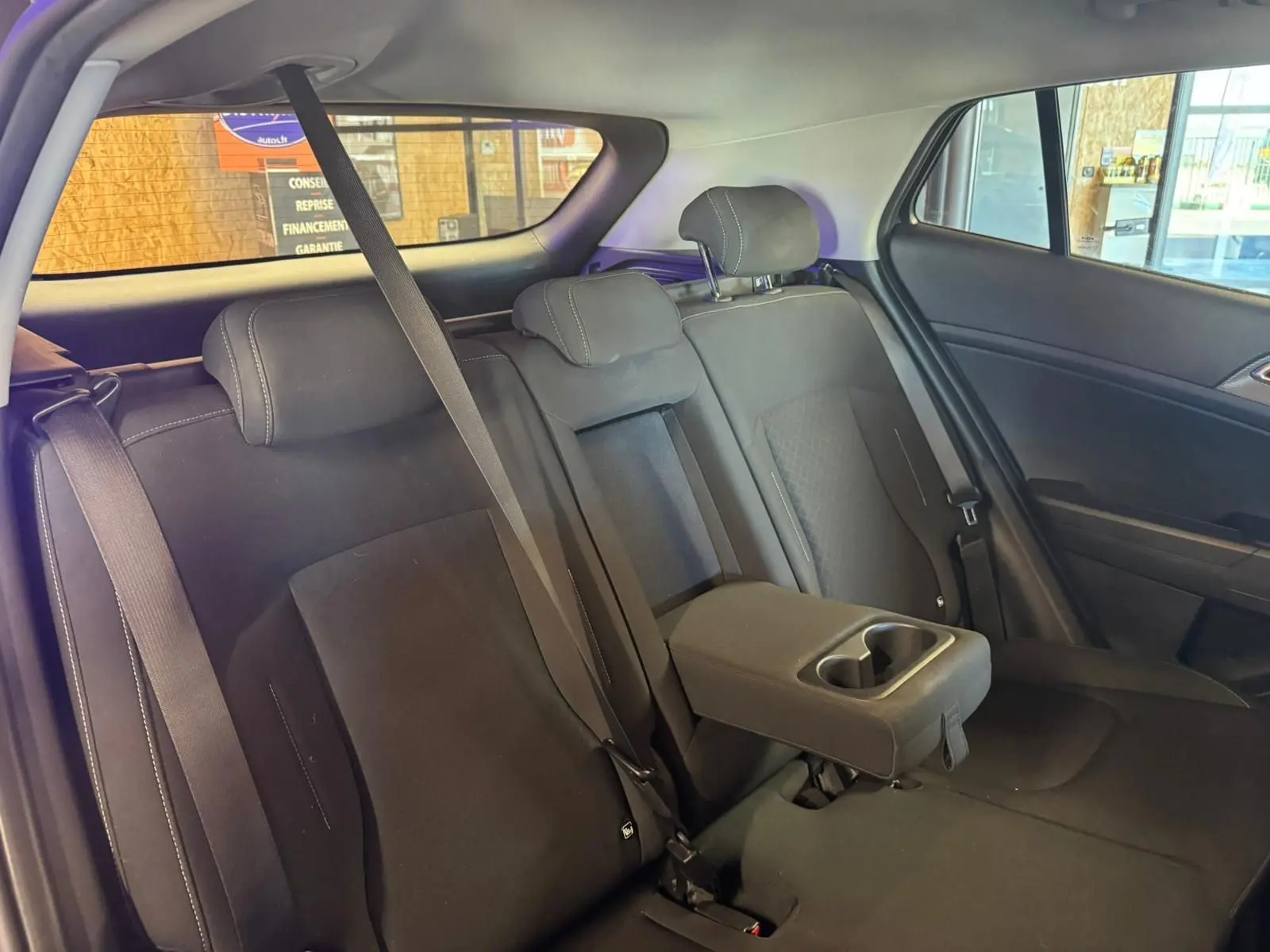 Vue intérieure de la banquette arrière noire du Kia Sportage 2022 avec accoudoir central et ceintures de sécurité visibles.