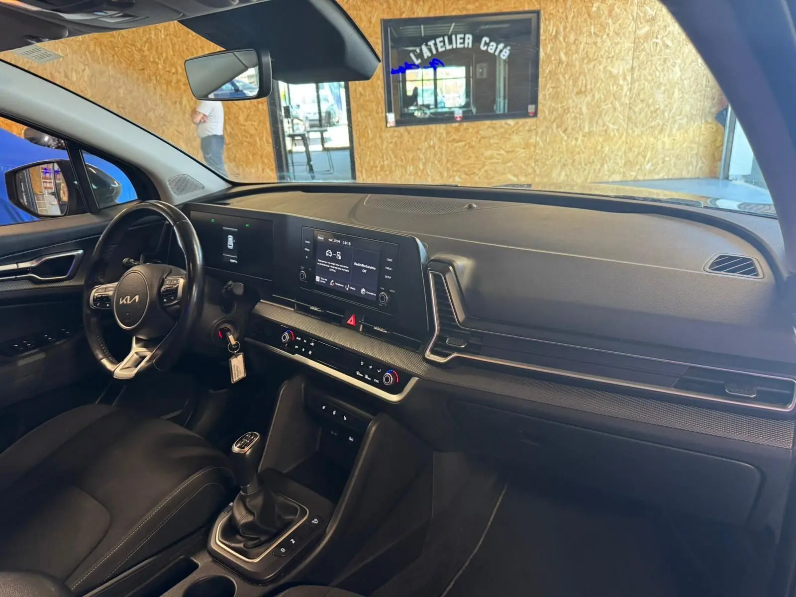 Intérieur noir du Kia Sportage 2022, vue côté conducteur sur tableau de bord moderne avec écran tactile et boîte manuelle.