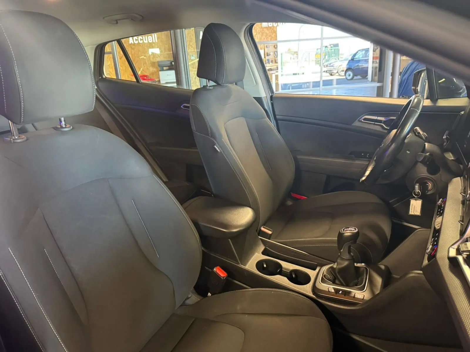 Vue intérieure côté conducteur du Kia Sportage noir 2022, mettant en valeur les sièges tissu noirs et la boîte manuelle.