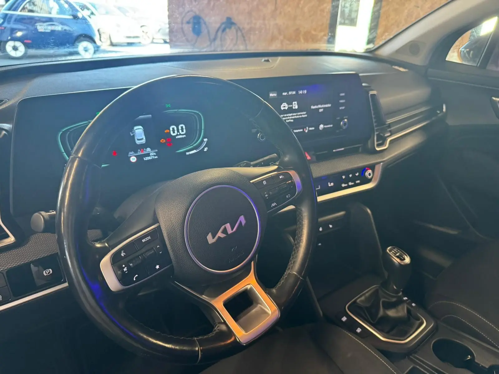 Vue intérieure côté conducteur du tableau de bord noir du Kia Sportage 2022 avec volant multifonction et boîte manuelle.