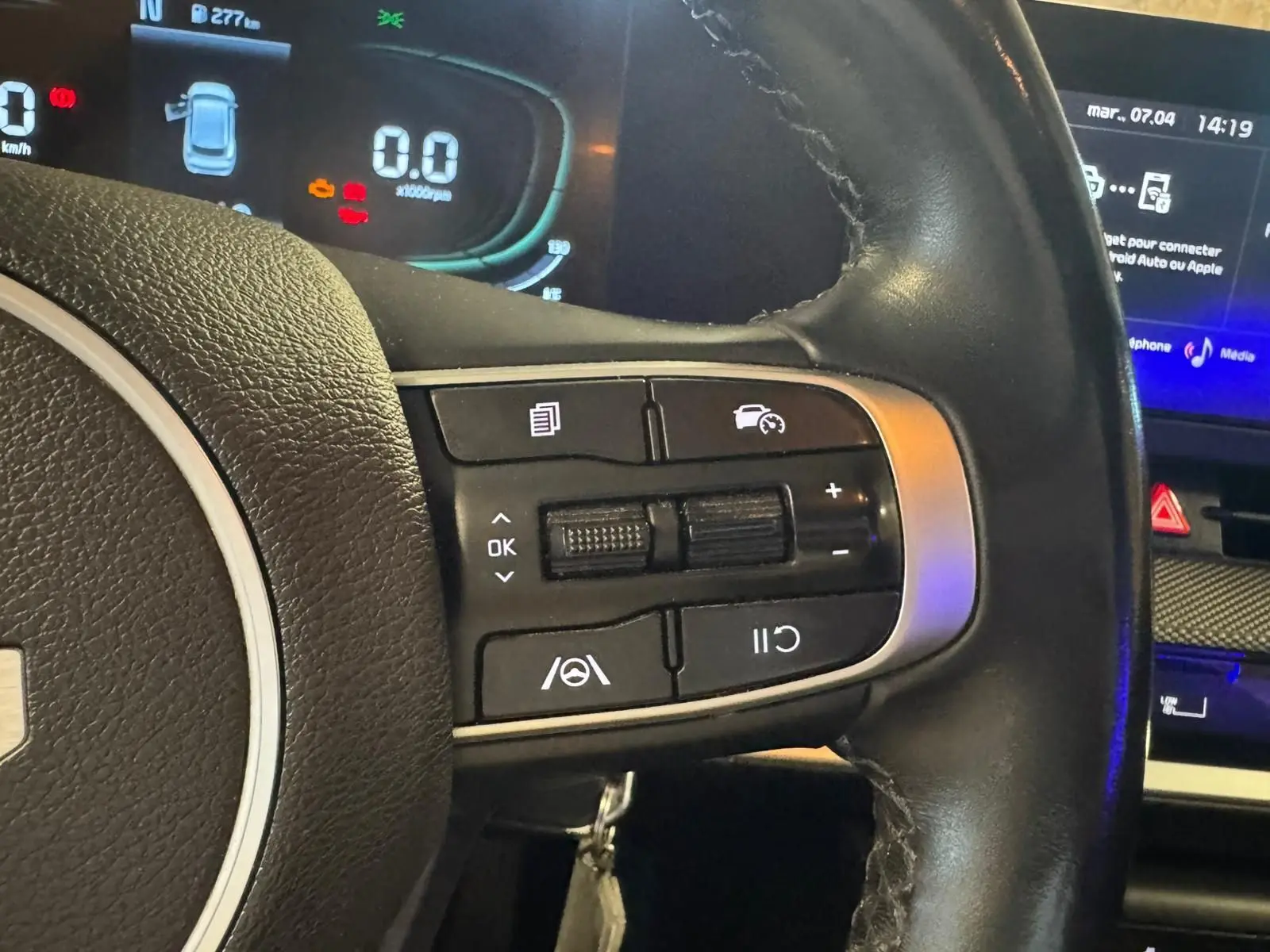 Gros plan sur le volant noir du KIA SPORTAGE 2022, montrant les commandes de régulateur de vitesse et tableau de bord digital.