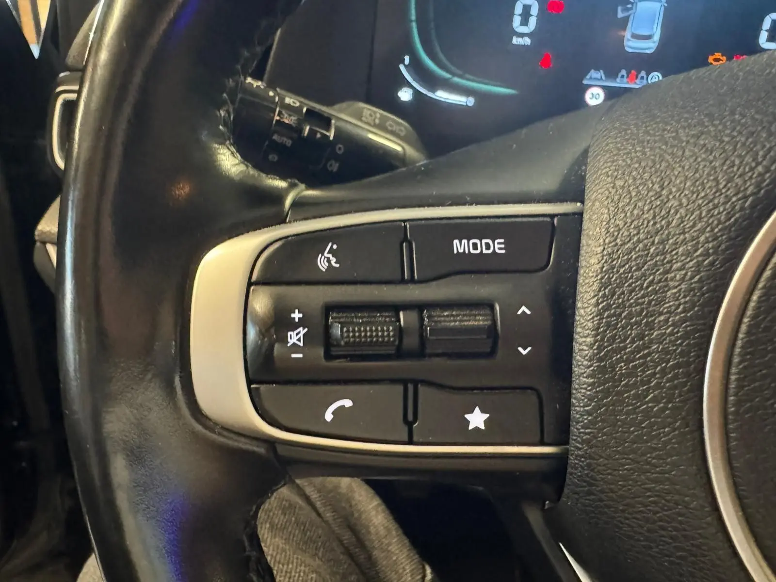 Gros plan sur les commandes gauche du volant noir du KIA SPORTAGE 2022, avec boutons de volume et mode audio visibles.