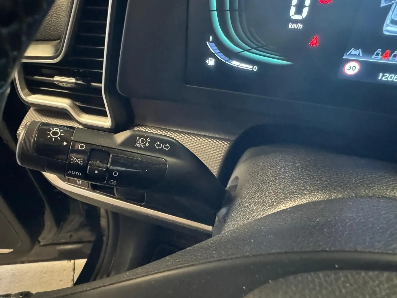 Gros plan sur la commande des phares et clignotants à gauche du volant du Kia Sportage noir, tableau de bord digital visible.