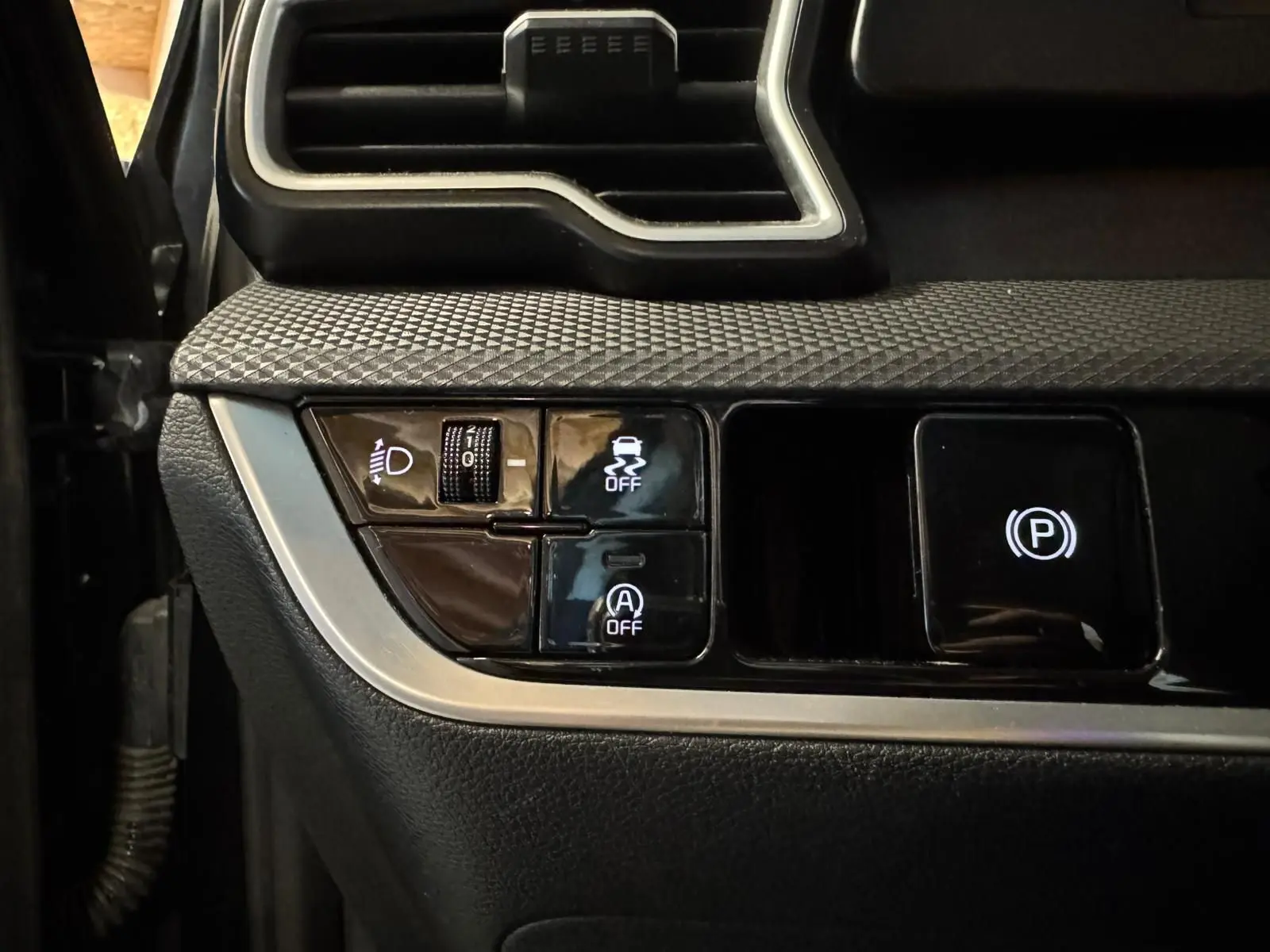 Détail des commandes côté gauche du tableau de bord du Kia Sportage noir 2022, avec boutons d'assistance et frein à main électronique.