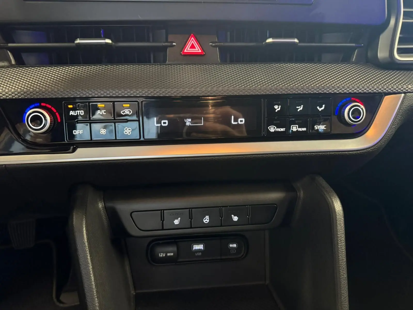 Tableau de bord du Kia Sportage 2022 noir, vue frontale centrée sur la commande de climatisation digitale et les boutons chauffants.