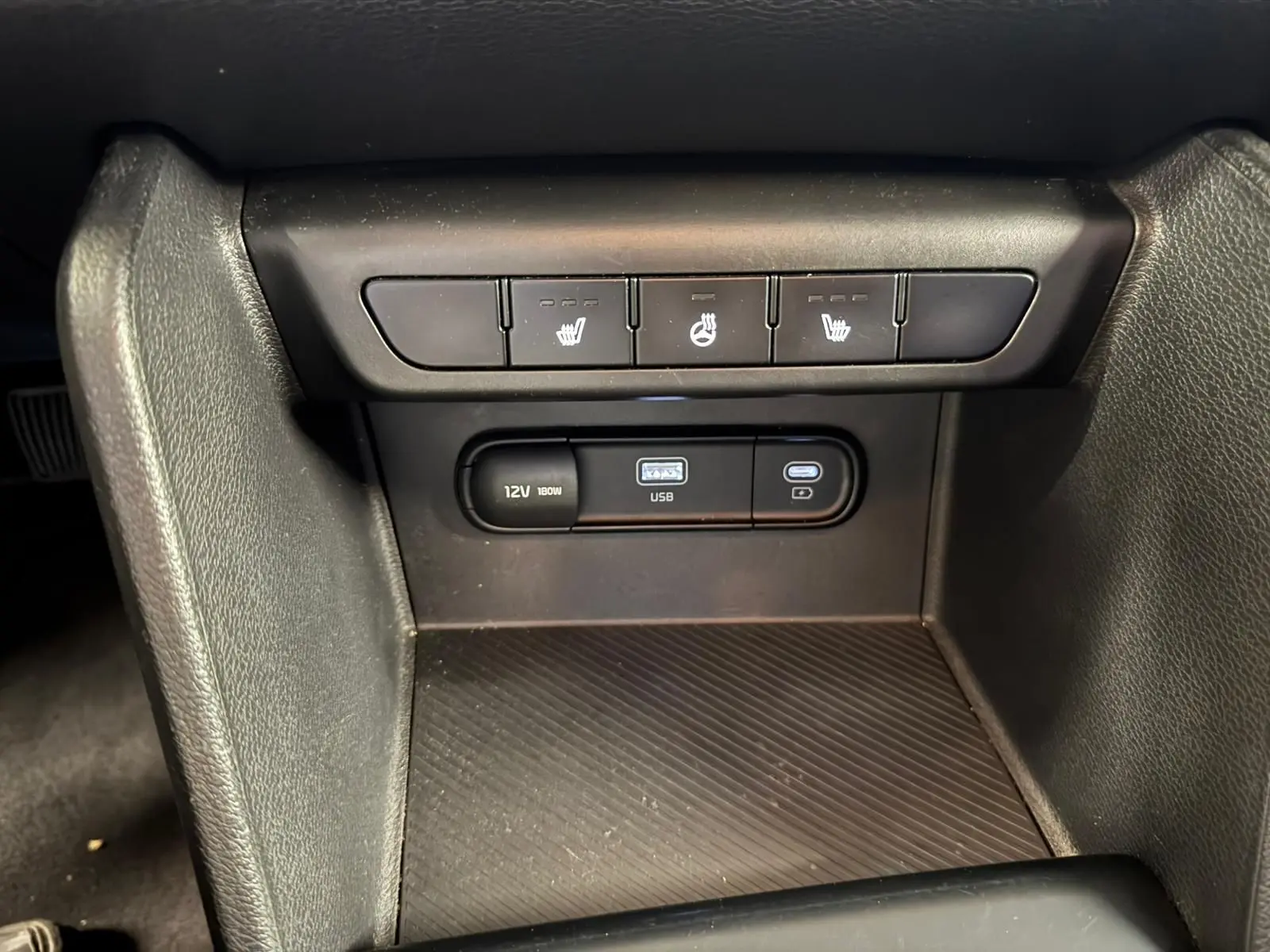 Vue rapprochée des commandes de sièges chauffants et des ports USB et 12V dans l’habitacle noir du Kia Sportage 2022.