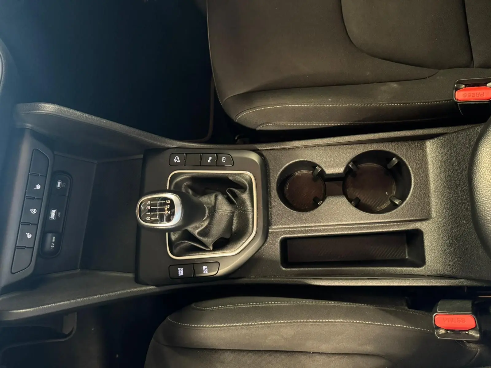 Vue plongeante sur la console centrale noire du Kia Sportage 2022, avec levier de vitesse manuel et porte-gobelets.
