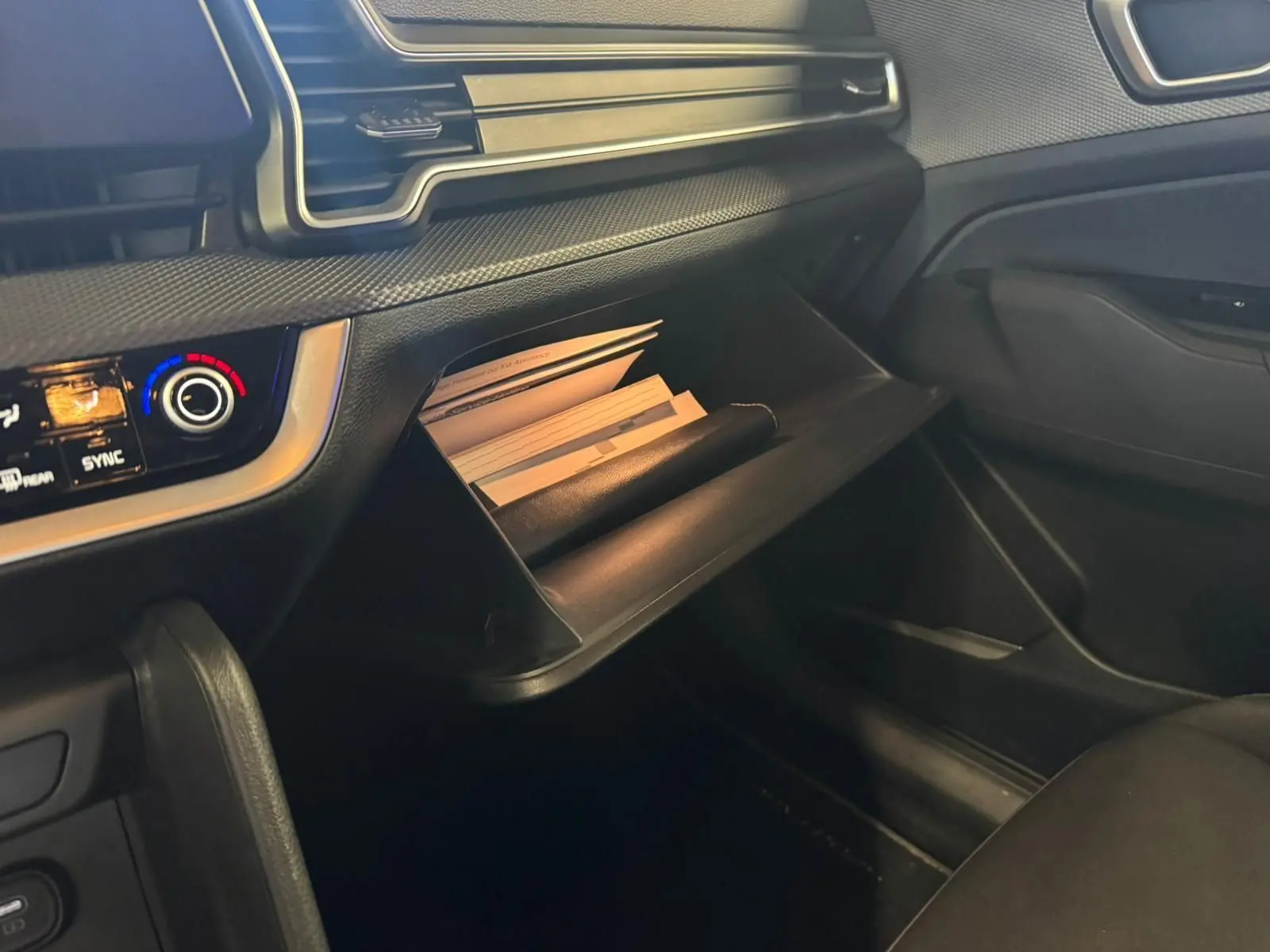 Intérieur noir du Kia Sportage 2022, vue côté passager sur la boîte à gants ouverte avec documents visibles.
