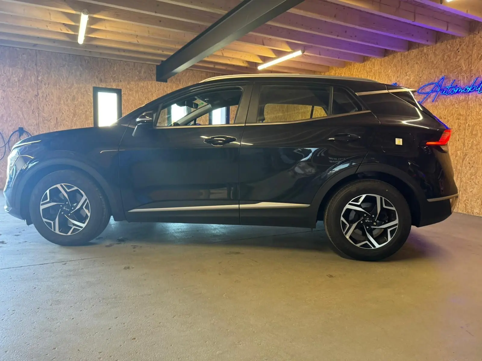 Vue latérale droite d'un KIA Sportage noir 2022, soulignant ses jantes alliage au design moderne dans un garage.