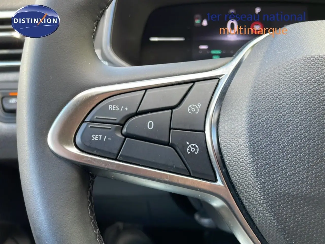 Gros plan sur les commandes au volant gauche de la Renault Clio gris schiste métal, avec régulateur de vitesse visible.