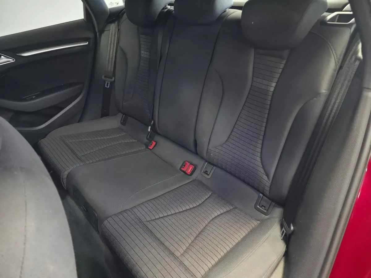 Vue intérieure arrière des sièges en tissu noir de l'Audi A3 Sportback rouge, avec ceinture de sécurité visible côté droit.