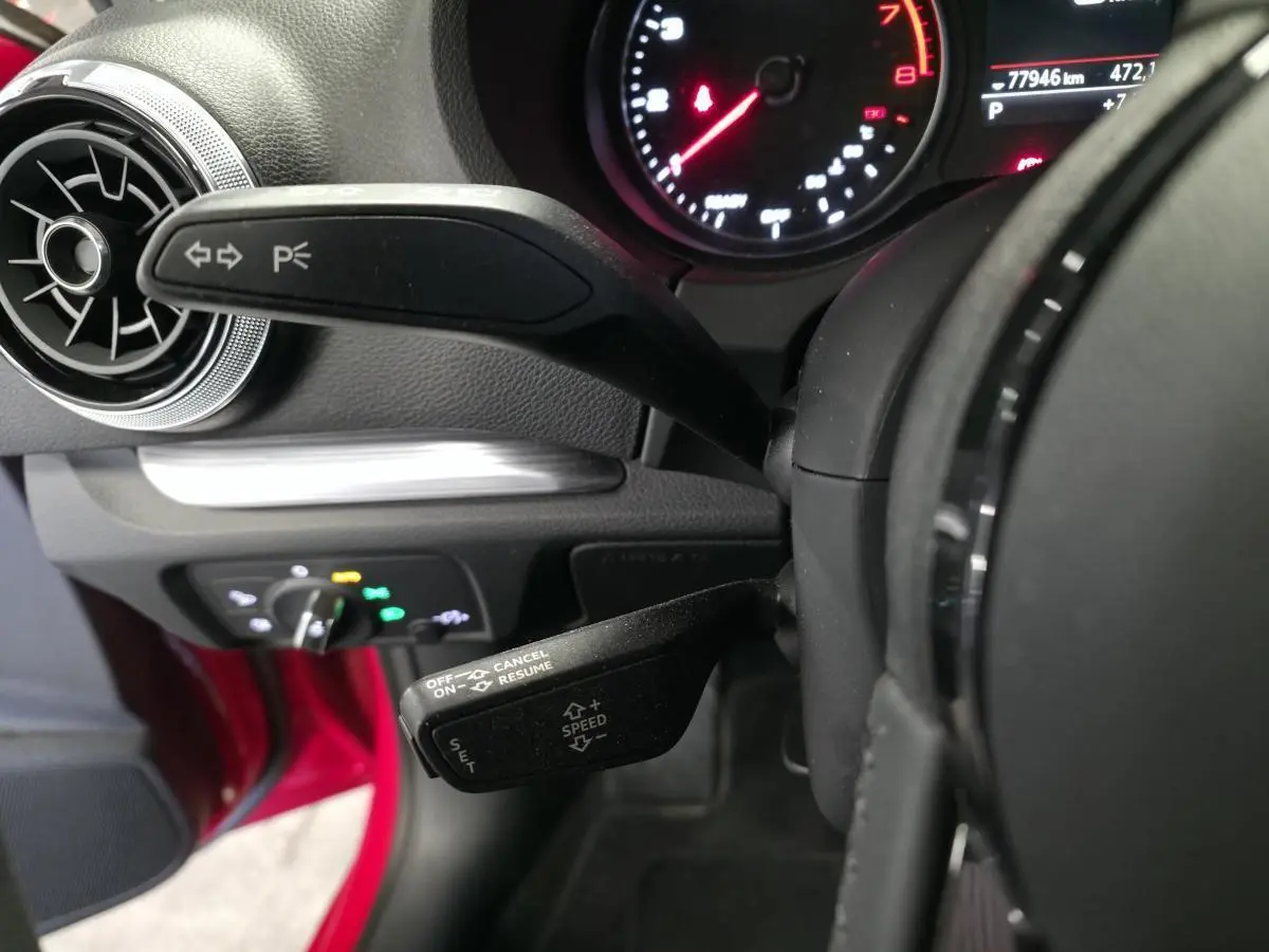Gros plan sur les commandes de volant et tableau de bord d'une Audi A3 Sportback rouge, avec compte-tours et affichage digital.